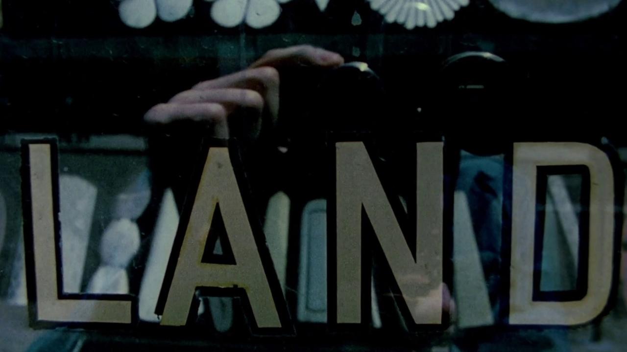 На этом кадре из «Лемма Цорна» (1970) изображено слово LAND, выведенное объёмными буквами на вывеске, в отражении стекла которой виден силуэт самого Фрэмптона с 16-миллиметровой кинокамерой в руках. Этот кадр относится ко второй, самой известной части фильма — 45-минутной алфавитной матрице. В ней Фрэмптон выстраивает циклический 24-кадровый ритм (соответствующий проекционной скорости 24 кадра в секунду), используя снятые на улицах Манхэттена и Бруклина вывески, знаки и надписи, расставленные в алфавитном порядке от A до Z (слова на букву L в этой последовательности как раз представлены вывесками вроде LAND). По мере развития ленты слова постепенно замещаются закольцованными бытовыми и абстрактными визуальными метафорами — от парки мяса и мытья рук до срубания дерева